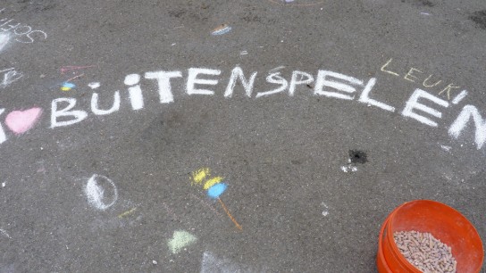Krijttekening op straat met de tekst "BUITENSPELEN" en een oranje emmer met stoepkrijt. (vergroot foto)